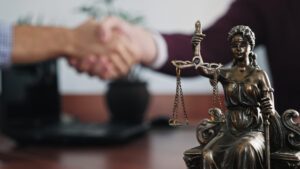 Statuette of Lady Justice on a table close-up, in the blurred background, a burn injury lawyer shakes hands with a client.